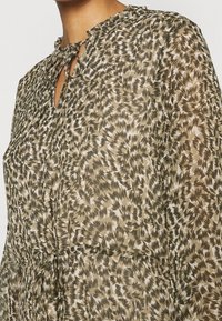 Långärmad blus i genomskinligt tyg, med ett mönster i olivgrön och beige abstrakt design, med nyckelhålsringning och detaljer med volanger vid kragen.