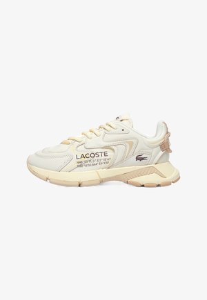 Baskets Lacoste crème avec des accents beiges, fermeture à lacets, semelle texturée, logo Lacoste et coordonnées géographiques imprimées sur le côté.