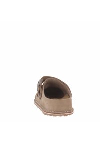 Scarpa slip-on in suede marrone con retro arrotondato, ritagli laterali, cuciture sottili e suola testurizzata per una presa sicura. Cinturino regolabile con accento metallico.
