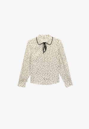 Blusa a maniche lunghe color crema con pois neri, con colletto e laccetti al collo. Il tessuto appare liscio con una leggera lucentezza.