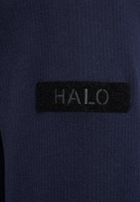 Granatowy, prążkowany materiał z czarną, fakturowaną, prostokątną łatą z napisem „HALO” w subtelnie wypukłych literach.