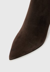 Talons aiguilles en suède marron avec un bout pointu, présentant une texture lisse et mate ainsi qu'une silhouette fine, conçues pour un look ajusté.