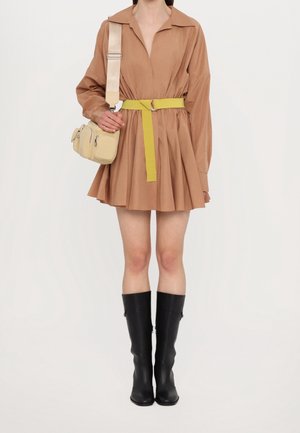 Brun langærmet kjole med indsnævret talje, gul bælte, sorte knæhøje støvler og en lille beige crossbody taske. Glat stofstruktur.