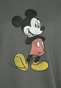 Grå t-shirt med en grafik av en cartoonfigur med svarta öron, ett leende ansikte, röda shorts och stora gula skor.