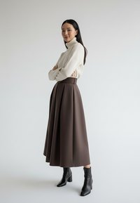 Kremowy sweter z prążkowanym golfem zestawiony z brązową plisowaną spódnicą z wysokim stanem oraz czarnymi botkami na obcasie. Prosty, elegancki design.