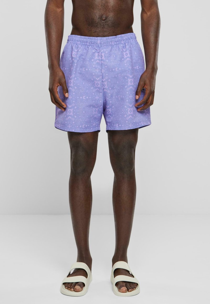 Shorts de bain violets avec un motif subtil, une taille élastique et une coupe droite. Associés à des sandales blanches à bout ouvert.