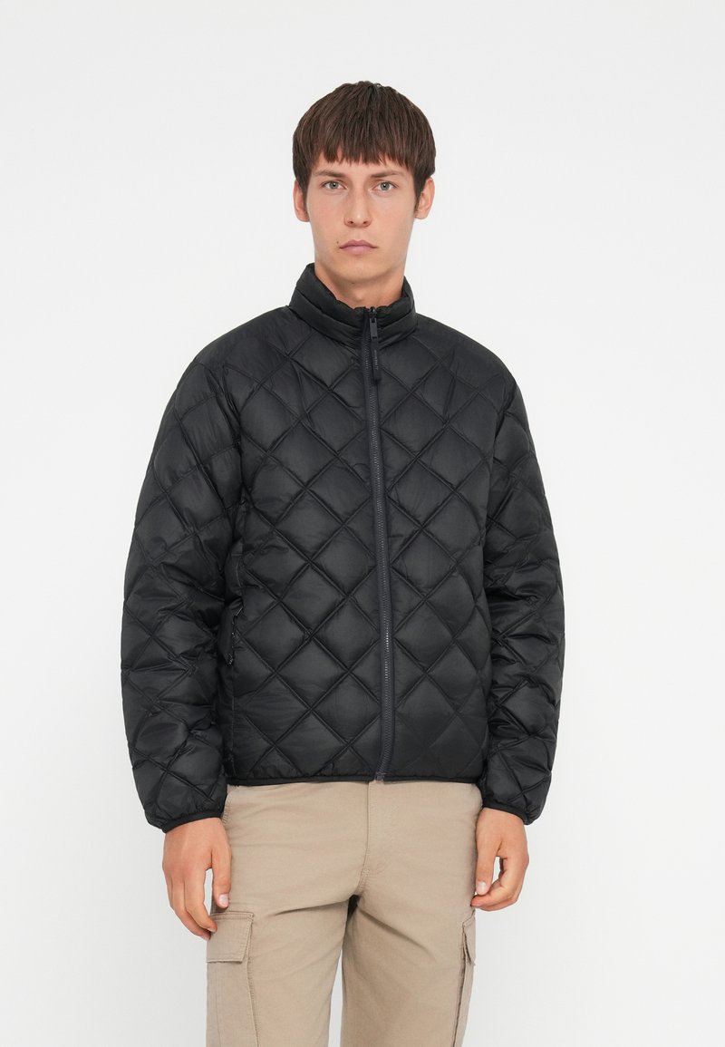 Giacca imbottita nera trapuntata con colletto alto, zip frontale e tasche laterali; presenta un motivo a diamante e una texture liscia.