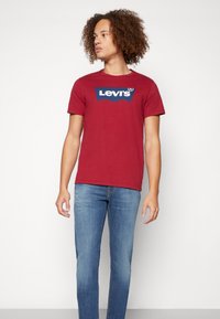 Rød bomulls T-skjorte med en blå Levi's-logo på brystet, kombinert med lyseblå denimjeans. Enkel design med rund hals og korte ermer.