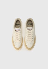 Baskets beiges avec une tige crème texturée, des détails perforés et des accents en daim beige. Comprend des lacets plats et une languette avec logo.