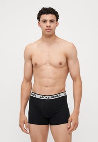 Fekete boxer alsónadrág puhán elasztikus derékkal, fehér logóval. Az anyag sima és rugalmas, növelve a kényelmet és a megfelelő illeszkedést.