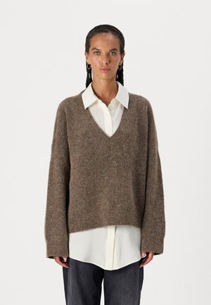 Brown knit sweater with a V-neck and long sleeves, layered over a white collared shirt. Soft, textured fabric with a loose fit.