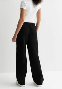 Zwarte wijde broek met een elastische tailleband, gemaakt van zachte stof. Heeft een gladde textuur en een relaxte pasvorm. Draagt met een aansluitend wit topje.