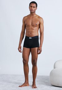 Boxer en coton noir avec une ceinture élastique logo, coupe ajustée et texture lisse, porté par un mannequin masculin dans un décor neutre.