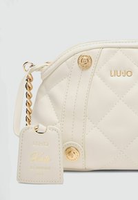 Weiße, gesteppten Handtasche aus Kunstleder mit goldfarbenen Beschlägen, Kettenriemen und einem abnehmbaren Anhänger mit dem eingeprägten Schriftzug "Kate Re-Edition".