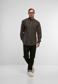 Graues Hemd mit spitzem Kragen und Brusttasche, kombiniert mit schwarzen Jeans und beigen Turnschuhen. Glatte Textur, normale Passform.