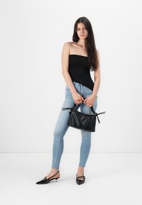 Svart teksturert håndveske med snøring, kombinert med lyseblå skinny jeans og en svart tube topp. Svart slingback-sko fullfører antrekket.