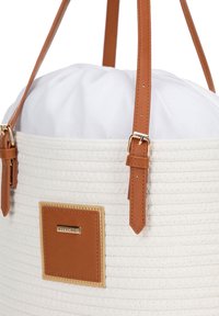 Borsa tonda intrecciata di colore bianco con manici in pelle marrone e una placca con logo dorato. L'interno presenta una fodera in tessuto bianco con un design arricciato.