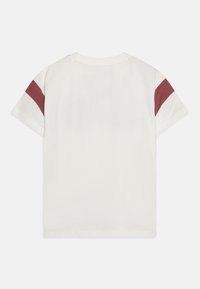 Camiseta de algodón blanca con rayas en los hombros en color burdeos, mangas cortas y cuello redondo. Textura suave y corte recto en el dobladillo.