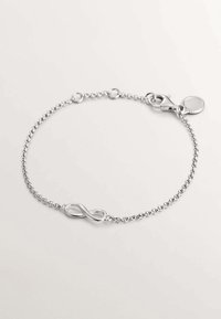 Pulsera de cadena de plata con un charm de símbolo de infinito, cierre de langosta y etiqueta redonda; textura suave con un acabado pulido.