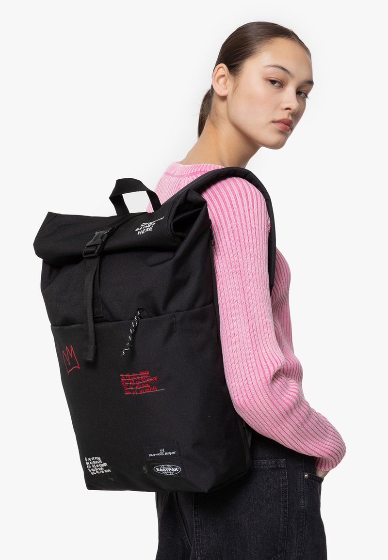 Svart rull-top ryggsäck med justerbara remmar, framficka, röda grafiska inslag och en hållbar tygstruktur.