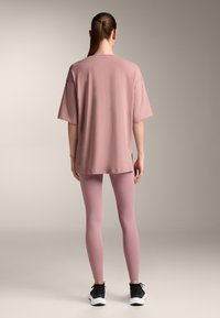 Relaxed-fit, pink t-shirt with short sleeves and side slits, paired with matching pink leggings. Footwear features black and white design accents.