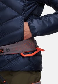 Marineblauwe gewatteerde jas met een grijze en oranje verstelbare riem met perforaties. De riem heeft een feloranje lus voor het bevestigen van uitrusting.