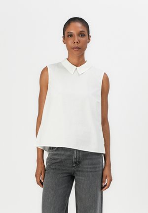 Chemise blanche sans manches avec un col pointu, présentant une coupe décontractée et une texture lisse, associée à un jean noir gris foncé taille haute.