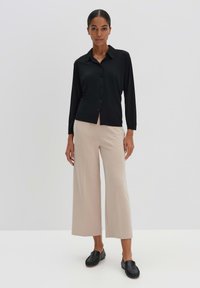 Chemise noire à boutons avec manches longues, pantalon beige à jambes larges, et chaussures noires à enfiler. Tissu lisse, coupe ajustée, et design minimaliste.