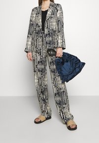 Blazer y pantalones a rayas en color marfil y azul marino, con un corte relajado. Top negro de canalé debajo. Los accesorios incluyen un bolso de satén en azul marino y sandalias.