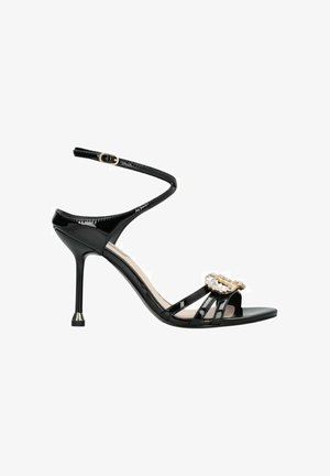 Sandalo stiletto in vernice nera con cinturino alla caviglia e fibbia dorata decorata con strass, tacco sottile e design a punta aperta.