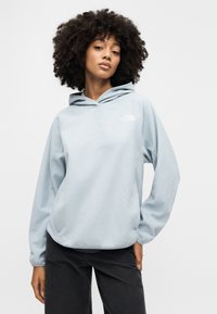 Φούτερ με κουκούλα από ελαφρύ γαλάζιο φλις με μακριά μανίκια και τσέπη καγκουρό μπροστά. Διαθέτει μικρό λευκό λογότυπο στο αριστερό μέρος του στήθους και κουκούλα με κορδόνι.