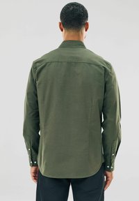 Chemise à manches longues vert olive, avec des poignets boutonnés, ourlet droit, détails de pattes de boutonnage au dos, fabriquée en tissu en coton doux.