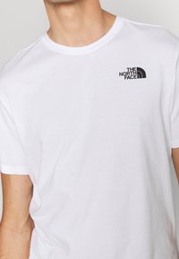 Bílá bavlněná tričko s krátkým rukávem. Na levé části hrudi má černé logo "THE NORTH FACE". Klasický design s kulatým výstřihem.
