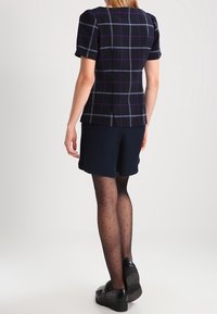 Navy plaid blouse with short puff sleeves, paired with navy shorts. Sheer black polka dot tights and black shoes complete the look.