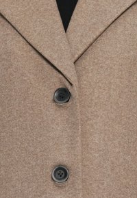Manteau en mélange de laine beige avec un col cranté, deux boutons noirs et une finition texturée. Vue en gros plan mettant en avant les détails des boutons.