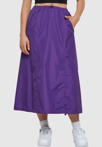 Lilla, lang nylon skjørt med elastisk midjebånd og justerbar snøring. Har sidelommer og en glatt tekstur.