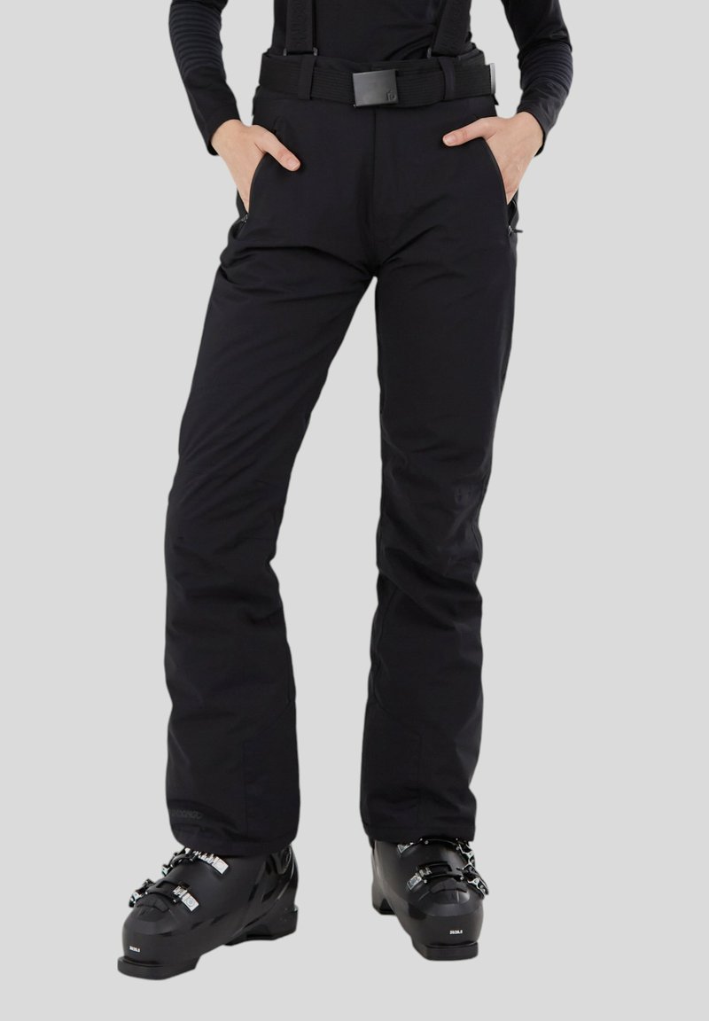 Schwarze Skihosen mit verstellbaren Trägern, Reißverschlusstaschen und strapazierfähigem Stoff; figurbetontes Design mit glatter Textur. Kombiniert mit schwarzen Skischuhen.