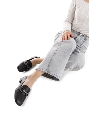 Zapatos de cuero negro con tacón cuadrado, puntera redonda y detalle decorativo de hebilla plateada. Combinados con jeans cortos de color gris claro.
