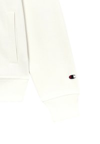 Sudadera blanca con una mezcla de algodón y poliéster. Presenta puños acanalados y un pequeño parche con el logo en la manga. Textura suave.