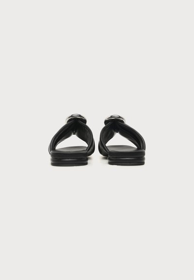 Paire de sandales plates en cuir noir avec larges brides et détails de boucle argentée, vue de dos sur fond blanc.