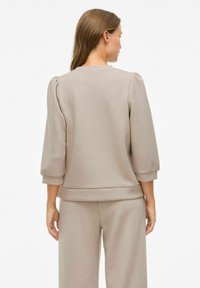 Felpa leggera beige chiaro con maniche a sbuffo a tre quarti e scollatura arrotondata, caratterizzata da un tessuto morbido e testurizzato e una vestibilità rilassata.