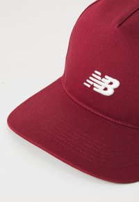 Red baseball cap made of smooth fabric with a flat brim. Features a white embroidered "NB" logo on the front.