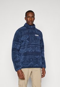 Fleece pulover tamno plave boje s geometrijskim uzorkom, visokim ovratnikom i polu-zatvaračem, s bočnim džepovima i logotipom na prsima.