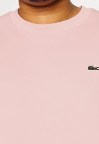 T-shirt a girocollo di colore rosa chiaro, realizzata in cotone; presenta un piccolo logo del coccodrillo verde Lacoste ricamato sul petto. Texture liscia.