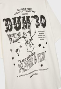 T-shirt en coton blanc avec un imprimé vintage noir de Dumbo accompagné de texte. Le design comprend des montgolfières et des étoiles.