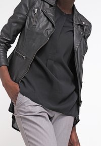 Černá kožená motocyklová bunda se stříbrnými zipy, nošená přes černý top, kombinovaná se světle šedými tailored kalhotami. Hladká textura a přiléhavý design.