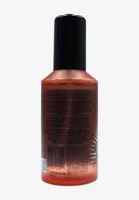 Bottiglia spray in plastica trasparente con una sfumatura arancione, tappo a pompa nero e etichetta degli ingredienti stampata in testo nero sul retro.