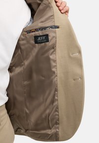 Beiger Blazer aus glattem Stoff mit satinierter Futter, und einer Innentasche mit einem gemusterten Akzent. Markenlabel innen sichtbar.