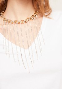 Collana in oro con fili pendenti in argento e perle trasparenti, caratterizzata da un design a strati che aggiunge texture e interesse visivo.