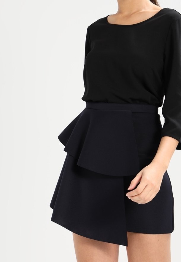 Blouse noire à manches trois-quarts associée à une jupe peplum bleu marine avec un design asymétrique en couches et une texture douce.